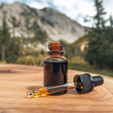 Shilajit oil in a small glass bottle with a dropper, dark resinous texture, rich amber glow, placed on a wooden surface with a natural mountainous backdrop