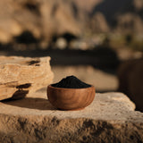 Shilajit powder in a small wooden bowl, with a natural background of Himalayan mountains or ancient rocks